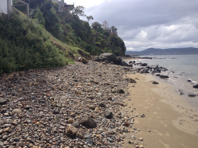 View north towards the volcanic rocks on Charles Darwin Cliff.  The foreshore is littered with dolerite and sandstone cobbles. In the middle ground are large dolerite boulders.