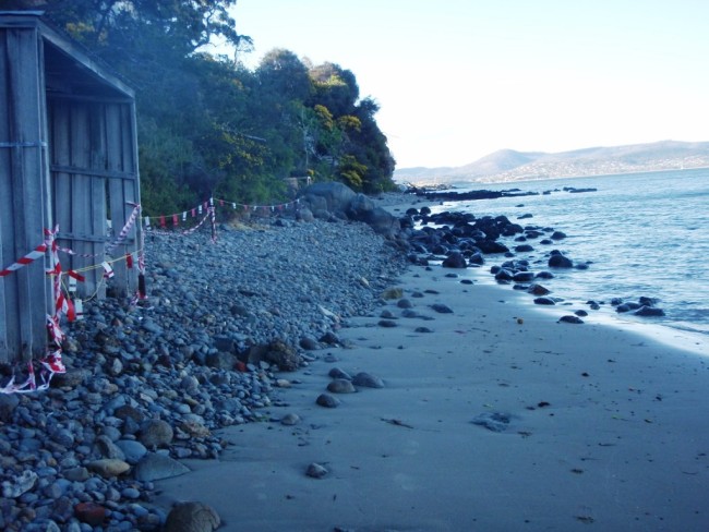 A view north towards Charles Darwin Cliff past large dolerite boulders in the middle ground. To the left of the boulders is an orange/brown/yellow outcrop exposed by storm waves.